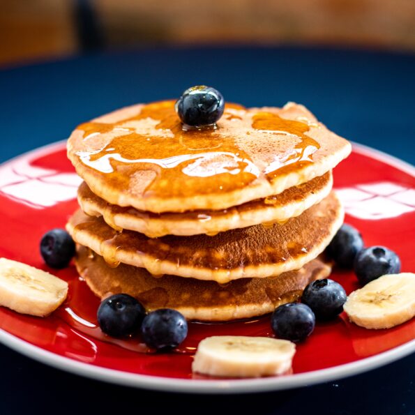 A stack of pancakes topped with blueberries and bananas on a red plate.
